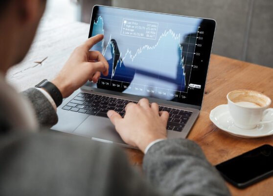 Cropped image of business man sitting by table in cafe Cropped image of business man sitting by the table in cafe and analyzing indicators on laptop computer